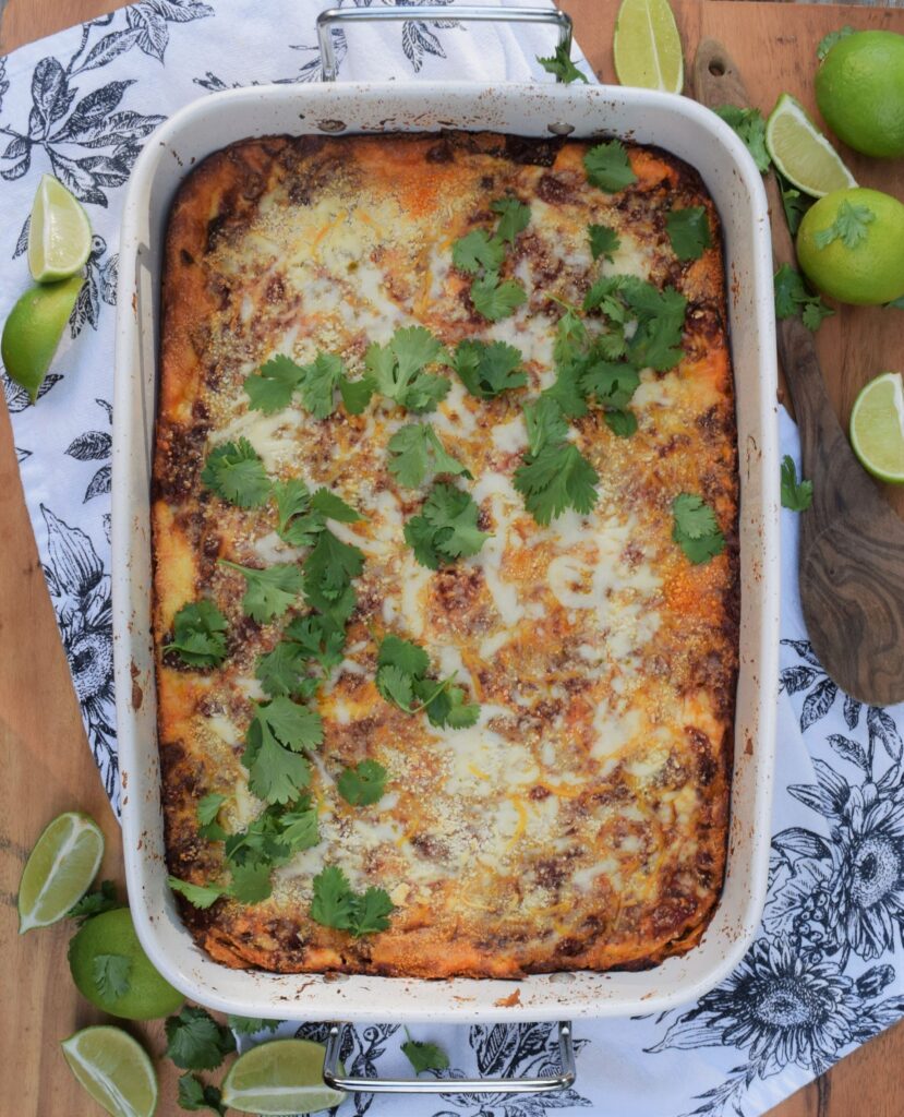 mexican lasagna comfort food spicy hispanic casserole cilantro limes on wood board with wooden spoon flat lay