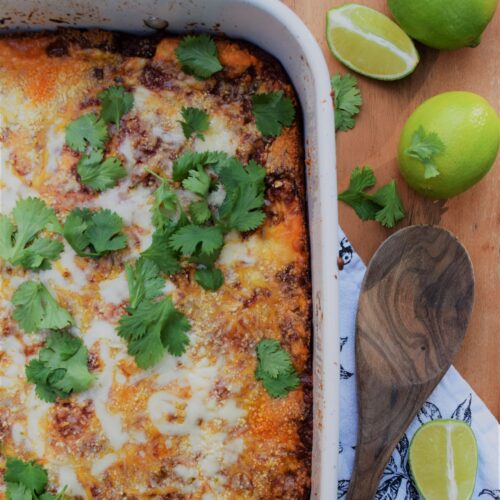 mexican lasagna comfort food spicy hispanic casserole cilantro limes on wood board with wooden spoon flat lay