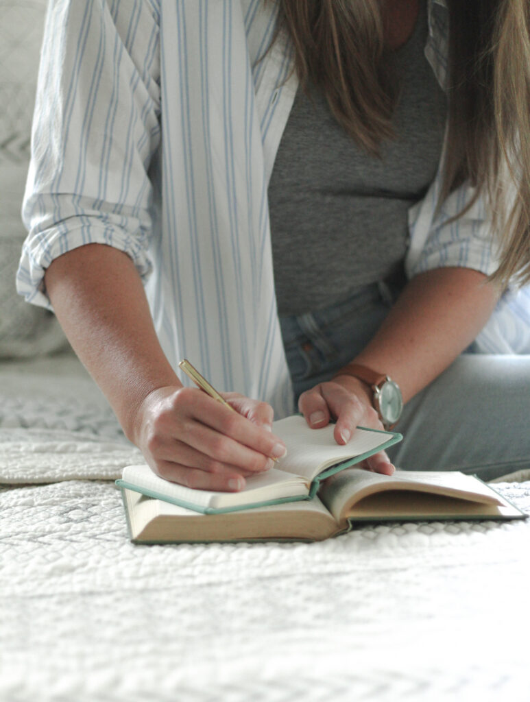 woman writing in journal on white quiltein morning light