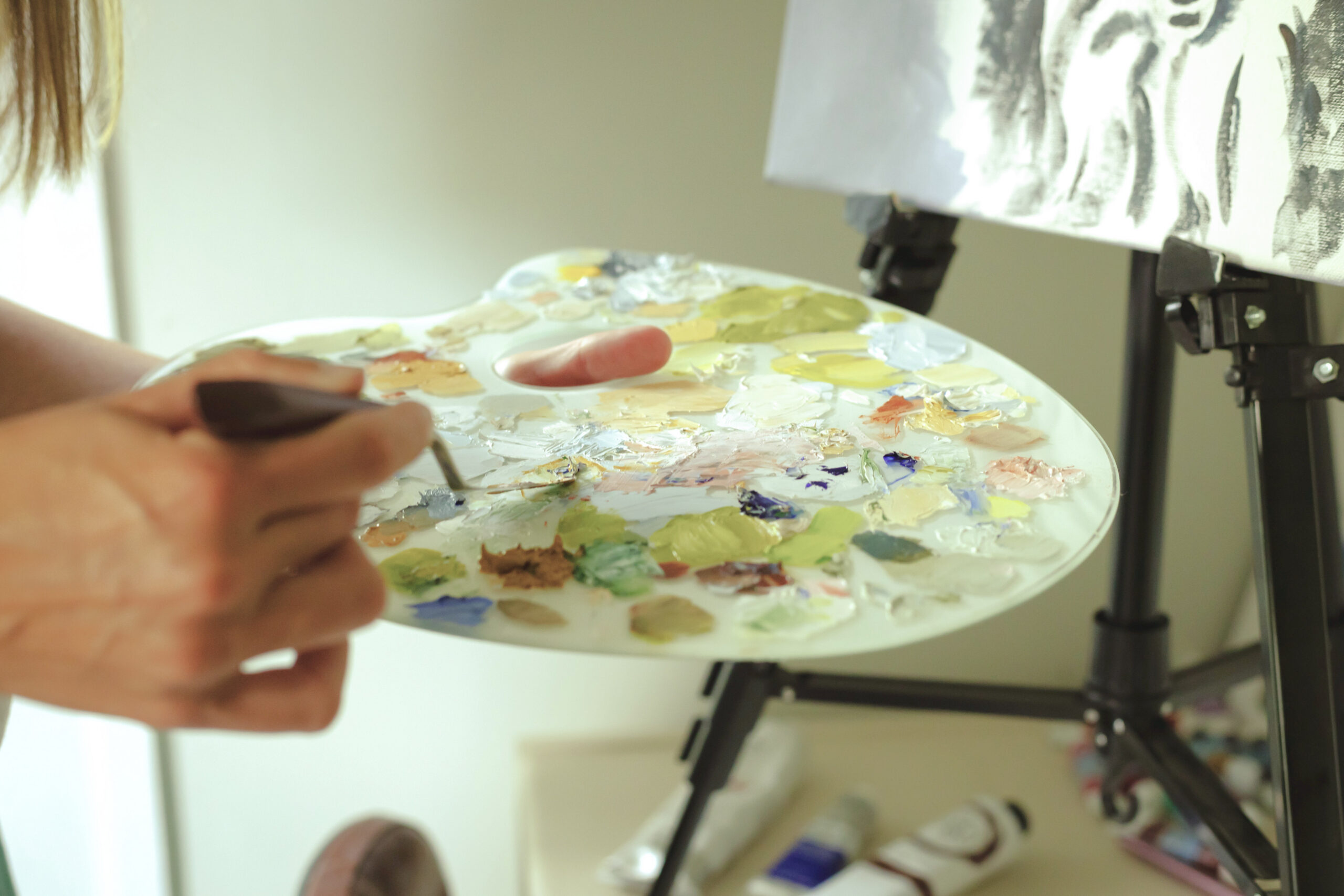 woman's hands holding a glass palette of pastel paints in her art studio